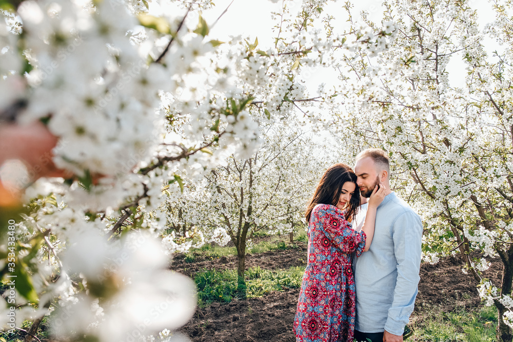 Loving couple hugging and walking. Lovestory in a blooming apple garden Loving couple hugging and walking. Lovestory in a blooming apple garden