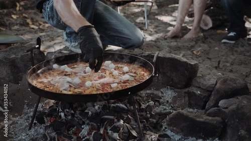 Closeup mans cook paella in a large frying pan outside, field kitchen, catering photo