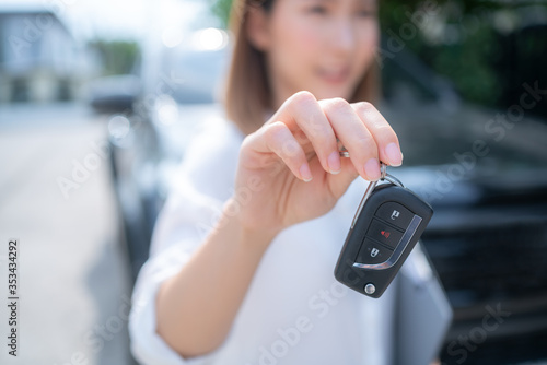 a woman picks up the car key to show in front of the car.