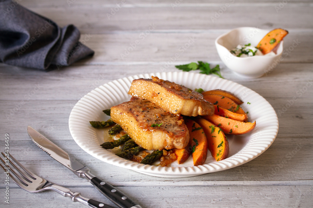 Juicy broiled pork chop steaks with asparagus, sweet potatoes and yogurt sauce. horizontal image Juicy broiled pork chop steaks with asparagus, sweet potatoes and yogurt sauce. horizontal image