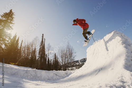 Snowboarder male jumping on quarter pipe snowboard in winter sunny day. Freestyle snowboard training