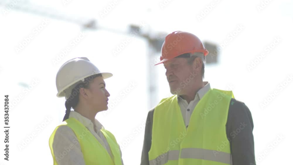 Two builders, a man and a young woman, are discussing work issues. Against the background of a crane. Two builders, a man and a young woman, are discussing work issues. Against the background of a crane.