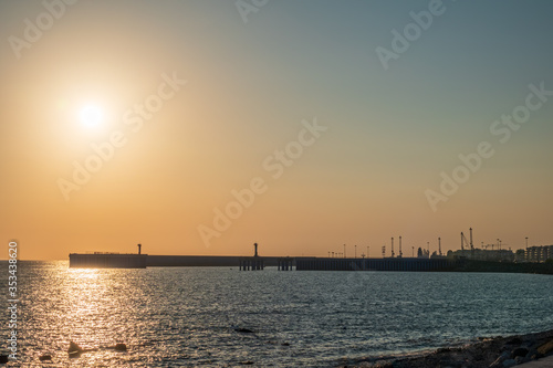 Clear sky and bright sunset at sea port with a breakwater and a lighthouse © Dmitrii Potashkin