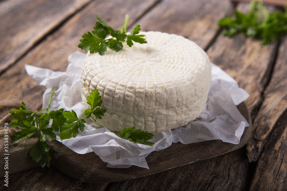 Suluguni cheese is cut into large pieces on a wooden round board. Garnished with parsley leaves, and pepper. Suluguni cheese is cut into large pieces on a wooden round board. Garnished with parsley leaves, and pepper.