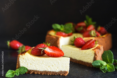 Fototapeta Naklejka Na Ścianę i Meble -  Slice of cheesecake with strawberries and mint on a dark background. Cheesecake New York. Advertising. Restaurant menu.