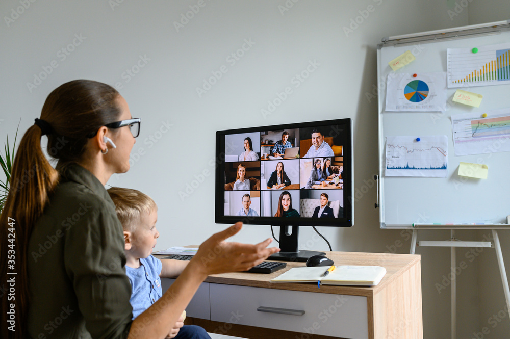 Back view of young mother in eyeglasses is talking online, she using lPC for video meeting with employees, cute baby boy sits on her laps. Busy mom works at home Back view of young mother in eyeglasses is talking online, she using lPC for video meeting with employees, cute baby boy sits on her laps. Busy mom works at home