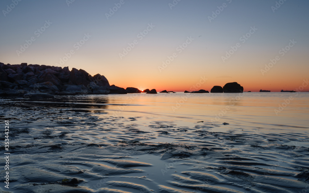 Southern coast of Finnish Gulf. Sand dunes with wave pattern. Baltic Sea water reflecting orange morning sky. Smooth transparent water, dark rocks. Blue hour turning to golden period. Estonia, Baltic Southern coast of Finnish Gulf. Sand dunes with wave pattern. Baltic Sea water reflecting orange morning sky. Smooth transparent water, dark rocks. Blue hour turning to golden period. Estonia, Baltic