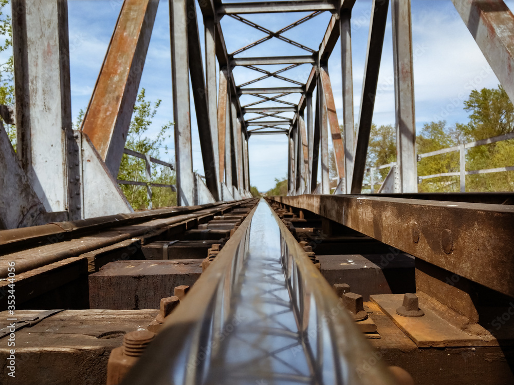 A rusted railroad bridge on a sunny day with cloudy blue sky on the background.