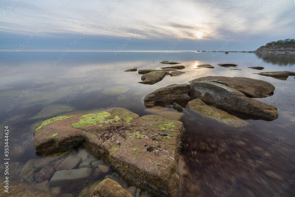 Southern coast of the Finnish Gulf. Rocks covered with green seaweed in the Baltic sea. Smooth transparent reflective water. Blue hour after sunset. Clouds concentrating in the middle. Estonia, Baltic Southern coast of the Finnish Gulf. Rocks covered with green seaweed in the Baltic sea. Smooth transparent reflective water. Blue hour after sunset. Clouds concentrating in the middle. Estonia, Baltic