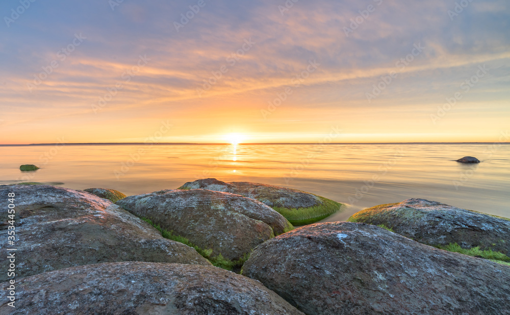 Southern coast of the Finnish Gulf. Rocks covered with green seaweed in the Baltic sea. Smooth transparent reflective water. Orange sunset markings under the low altitude clouds. Estonia, Baltic