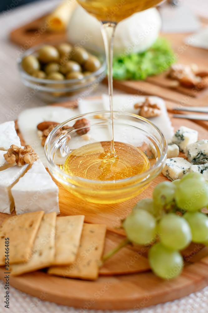 Chef pours honey. Cheese mix on a wooden plate decorated with grapes, nuts, salad and olives with cheese knifes Chef pours honey. Cheese mix on a wooden plate decorated with grapes, nuts, salad and olives with cheese knifes