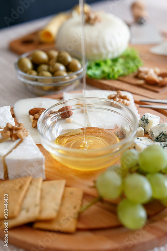 Chef pours honey. Cheese mix on a wooden plate decorated with grapes, nuts, salad and olives with cheese knifes 