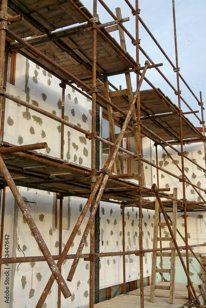 Thermal insulation of house wall with polystyrene. Picture of a scaffolding near familyhouse Thermal insulation of house wall with polystyrene. Picture of a scaffolding near familyhouse