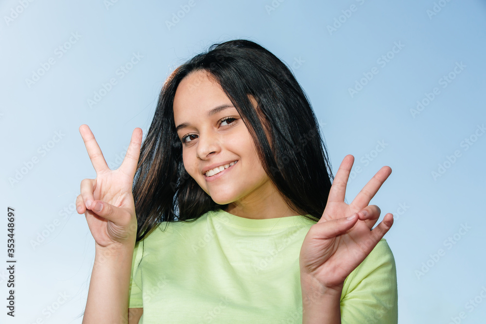 Portrait of a smiling happy woman showing victory sign and looking at camera on the blue background. Portrait of a smiling happy woman showing victory sign and looking at camera on the blue background.