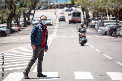 Uomo vestito casual con giacca in jeans e mascherina facciale protettiva , attraversa le strisce pedonali in pieno centro di una città photo
