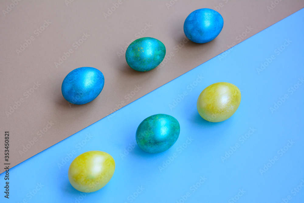 Bright blue, yellow and green eggs lie diagonally on light blue and gold paper. View from above. Holiday concept. Bright blue, yellow and green eggs lie diagonally on light blue and gold paper. View from above. Holiday concept.