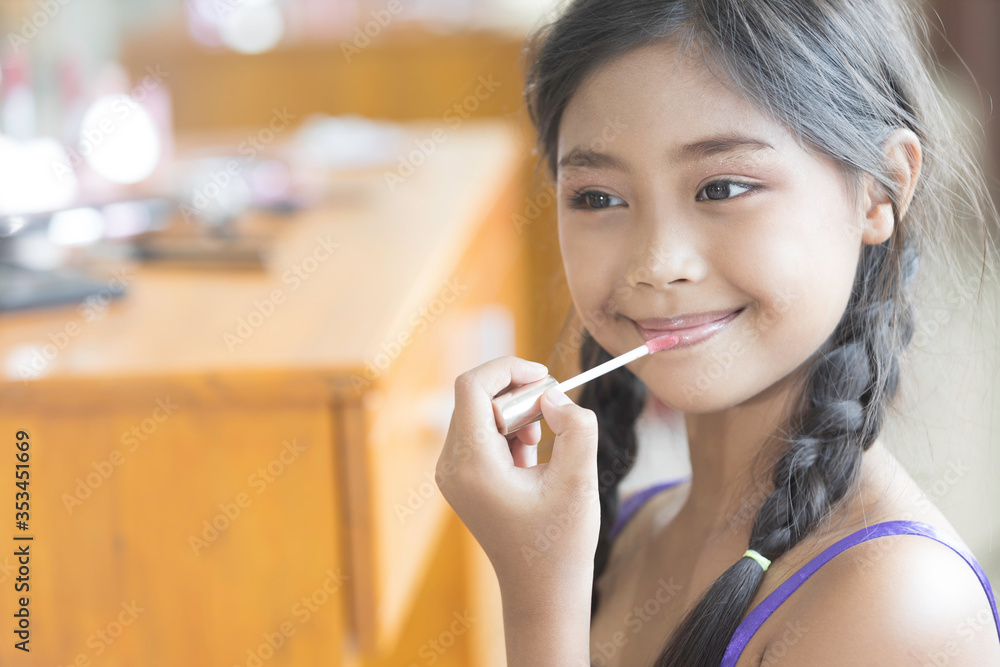 A cute long-haired Asian schoolgirl is using lipstick to apply lip makeup during a makeup lesson. A cute long-haired Asian schoolgirl is using lipstick to apply lip makeup during a makeup lesson.