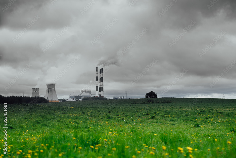the concept of global warming. the power plant pollutes the environment with emissions from pipes against a background of black sky and blooming meadows
