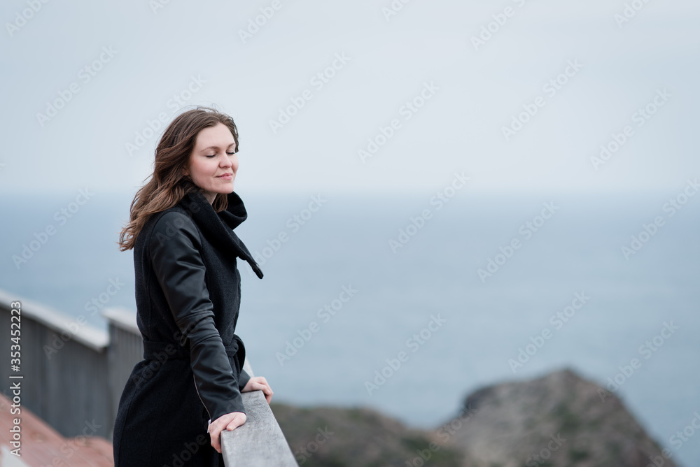woman leaning against the railing of the cliff while enjoying the views of the sea woman leaning against the railing of the cliff while enjoying the views of the sea