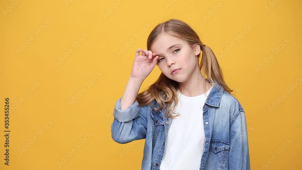Little sad blonde kid teen teenager girl 12-13 years old in denim jacket white t-shirt posing isolated on yellow background studio People childhood lifestyle concept Looking camera tired want to sleep Little sad blonde kid teen teenager girl 12-13 years old in denim jacket white t-shirt posing isolated on yellow background studio People childhood lifestyle concept Looking camera tired want to sleep