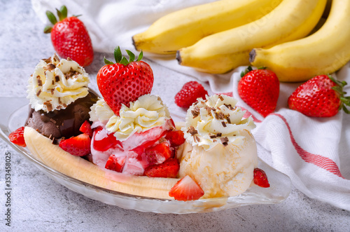 Sweet homemade banana split sundae with chocolate vanilla and strawberry ice cream on glass bowl, decoration topping fresh strawberries.