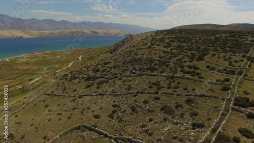 Aerial panning shot of plants and stone walls by sea against sky, drone flying forward over green landscape on sunny day - Pag, Croatia photo