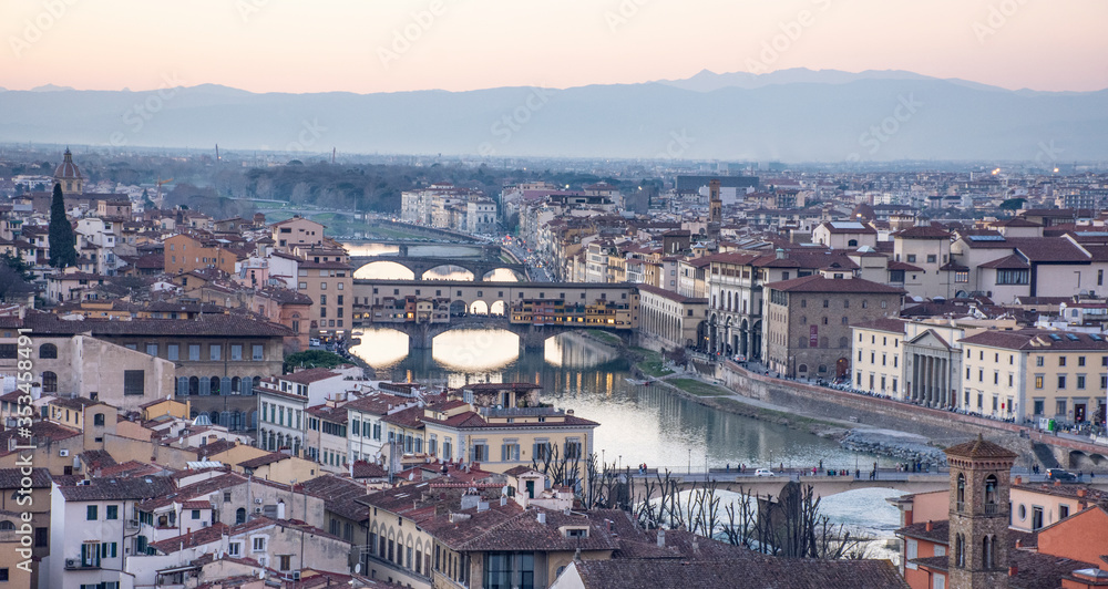 Vista de ciudad de Florencia atravesada por río en el atardecer con colinas de fondo