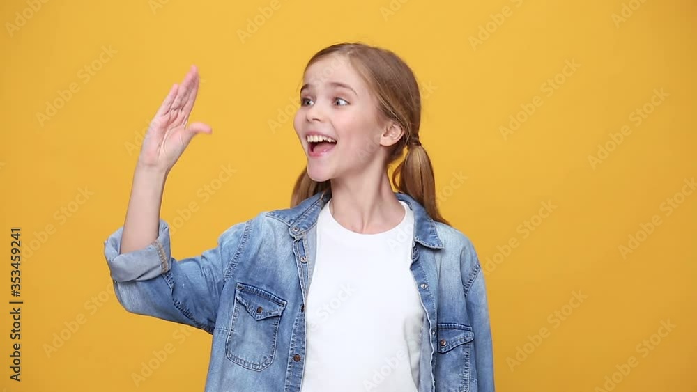 Little fun kid girl 12-13 years old in denim jacket white t-shirt posing isolated on yellow background studio People childhood lifestyle concept play showing talking to each other hands fooling around Little fun kid girl 12-13 years old in denim jacket white t-shirt posing isolated on yellow background studio People childhood lifestyle concept play showing talking to each other hands fooling around