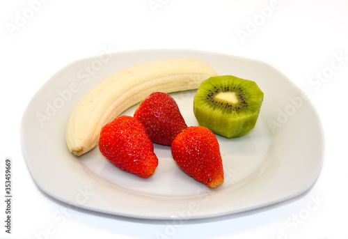 peeled banana strawberry and kiwi on a white plate on a white background