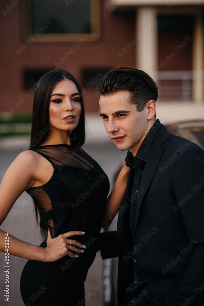 A young stylish couple in black stands near the car at sunset. Fashion and style A young stylish couple in black stands near the car at sunset. Fashion and style