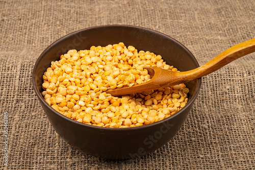 Yellow split peas in a ceramic bowl on a background of coarse-textured burlap. Traditional cereals for making soups and porridge. Close up.