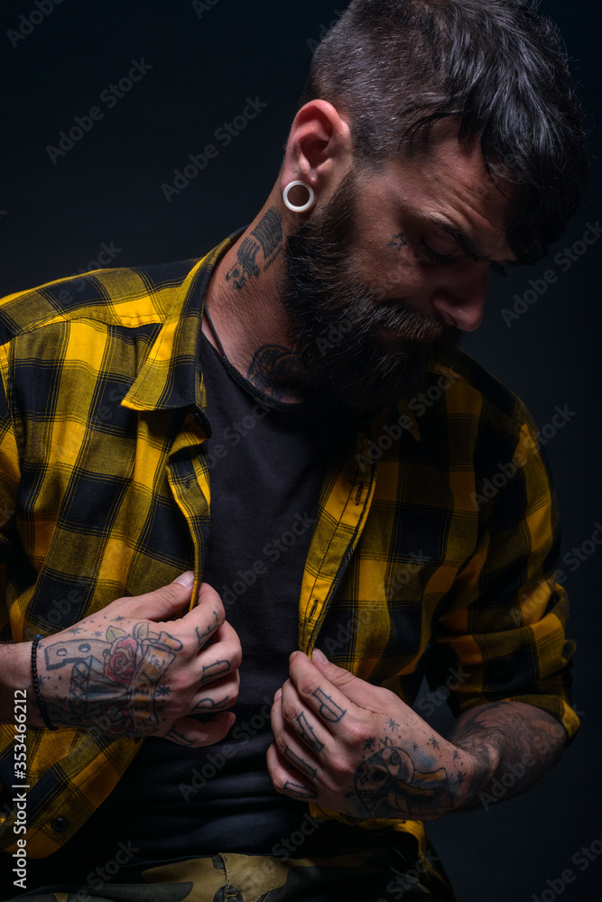 Close up portrait of a bearded man with tattoos on his hands and neck wearing yellow black shirt.