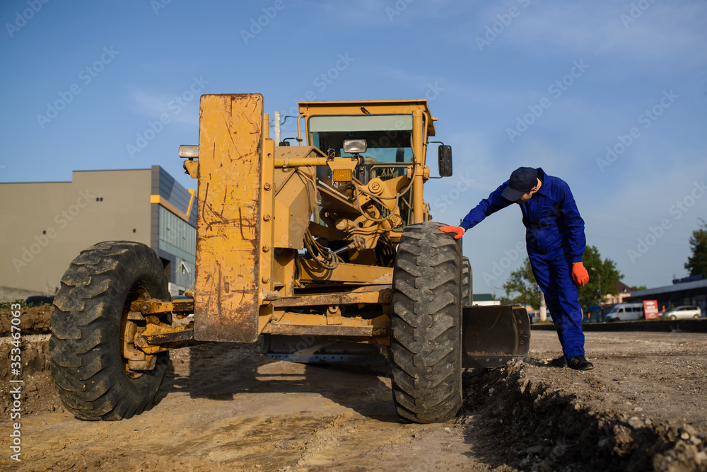 young man contractor builder in blue overalls is looking to the bulldozer wheel. young man contractor builder in blue overalls is looking to the bulldozer wheel.