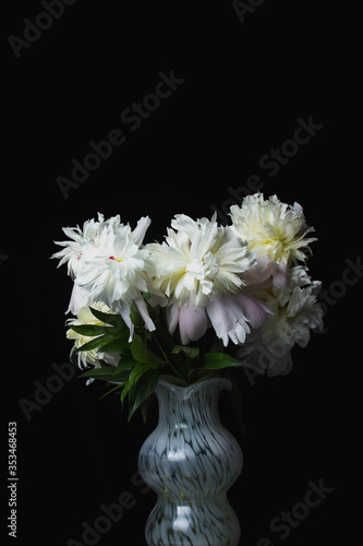 White vase with white peonies on a black background.