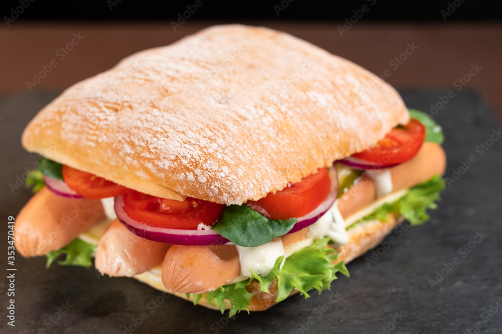 White bun with sausages and vegetables. Snack with a sandwich with sausages. White bun with sausages and vegetables. Snack with a sandwich with sausages.