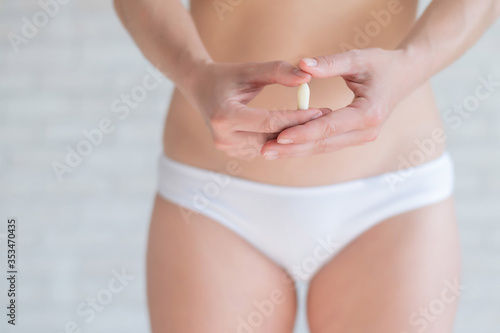 Faceless Caucasian woman in white panties and with a bare belly holds a healing candle. Girl demonstrates anal or vaginal suppository. Prescription from a gynecologist for women's health.