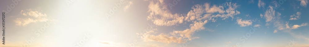 Warm sunny blue sky with fluffy clouds. Sunset sunlight illuminates the sky in sunset time. Beautiful ultra-wide panoramic background of atmosphere - obrazy, fototapety, plakaty 