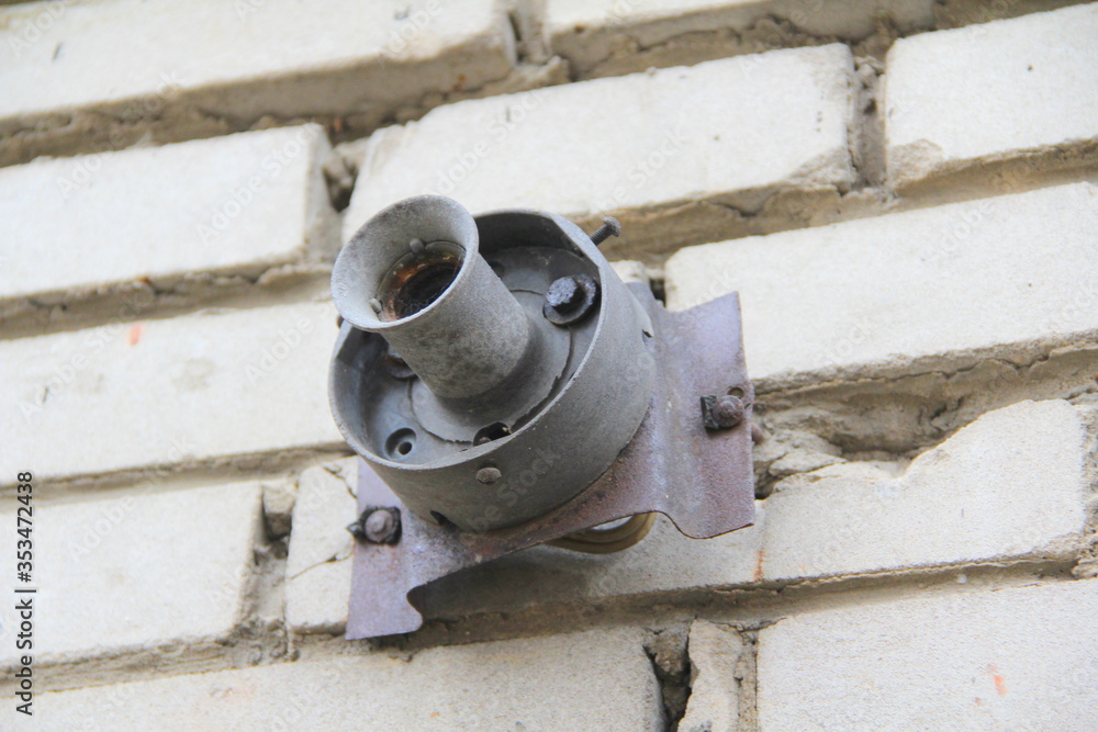 An old rusty cartridge for a street lighting lamp on a white brick wall. Electric equipment. An old rusty cartridge for a street lighting lamp on a white brick wall. Electric equipment.