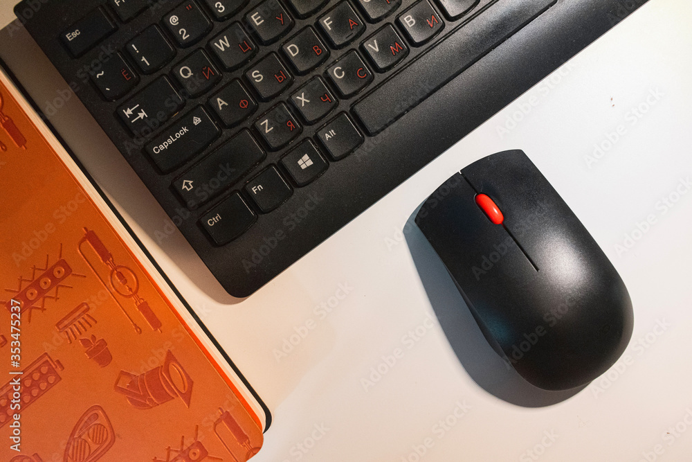 .Orange diary and black keyboard on a white table, top view. A mouse and keyboard next to the orange diary. .Orange diary and black keyboard on a white table, top view. A mouse and keyboard next to the orange diary.