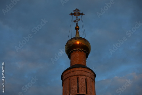 The dome of an Orthodox Church with a Christian cross against a blue sky with clouds at dusk.Bright sun glare spot on metal from the sun at sunset.Background image from bottom to top.Russia
