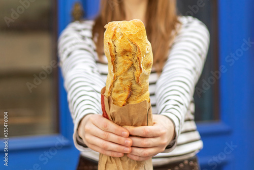 Close up of female hands holding fresh french baguette. In the background a beautiful blue door.