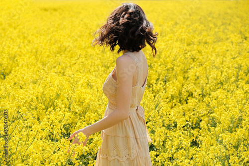 Back view of a pretty young girl in dress in field with yellow flowers on sunny summer day. © photoguns