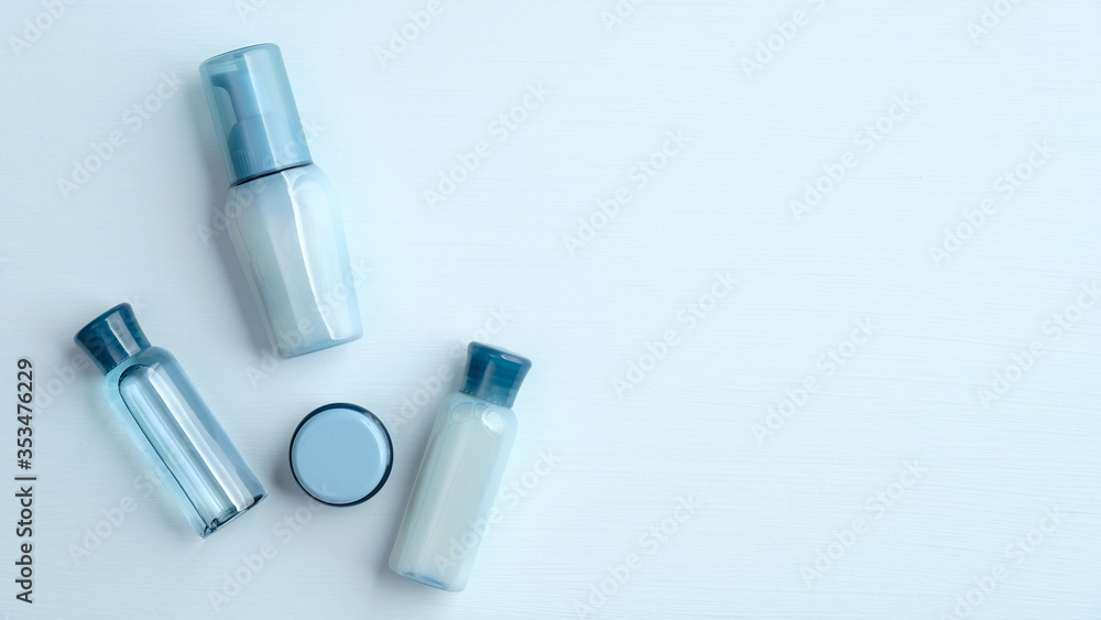 Fototapeta premium Set of natural organic SPA cosmetic products on blue background. Flat lay, top view transparent cosmetic bottles and cream jar. Banner mockup for beauty salon.
