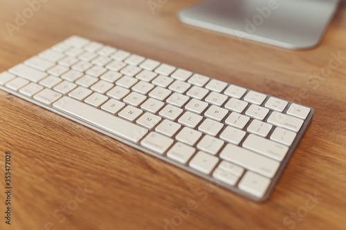 Close-up of modern white wireless keyboard on wooden table. Workplace concept. Selective focus