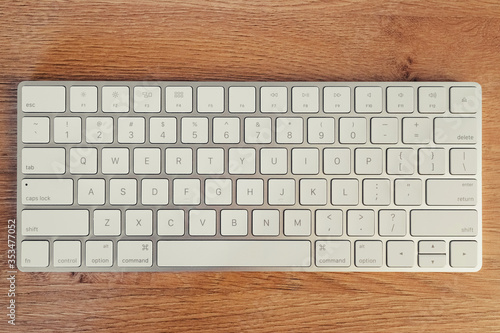 Close-up of modern wireless keyboard on wooden table background. Workplace. Top view