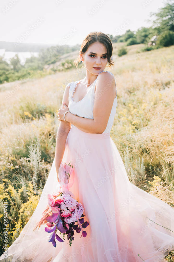 Bride in a luxurious white and pink wedding dress in nature at sunset