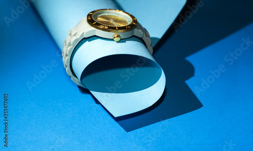 Wristwatch with silicone strap and gold clock face on blue background. Stylish and modern, unisex.