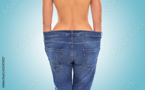 Slender girl in big jeans on a blue background. Losing weight.
