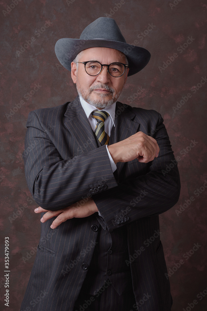 Señor maduro posando para la cámara con un traje de color café oscuro con rayas y sombrero