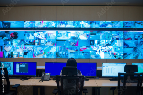Female security guard sitting back and monitoring modern CCTV cameras in a surveillance room.